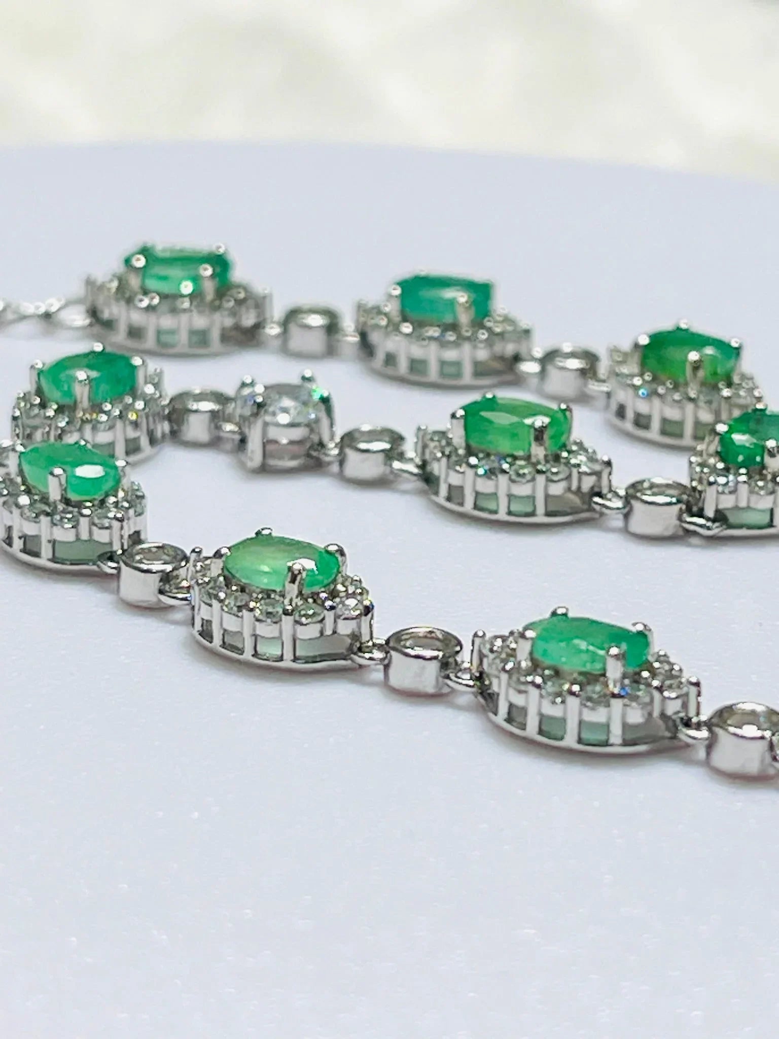 Close-up of handcrafted sterling silver bracelet with rhodium plating, showing oval Colombian emeralds in clear halo settings.