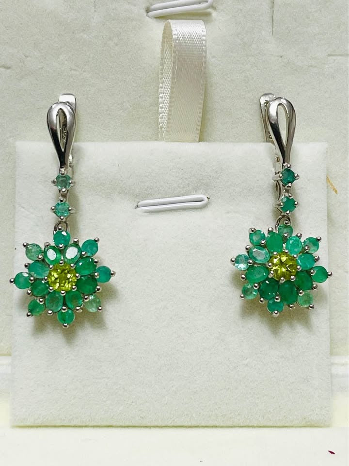 Pair of natural Colombian emerald and peridot flower drop earrings in sterling silver, displayed on a white stand.