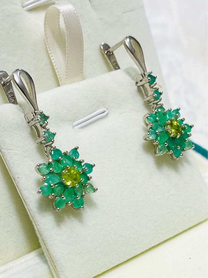 Angled view of natural Colombian emerald floral earrings with peridot accents, set in shining silver.