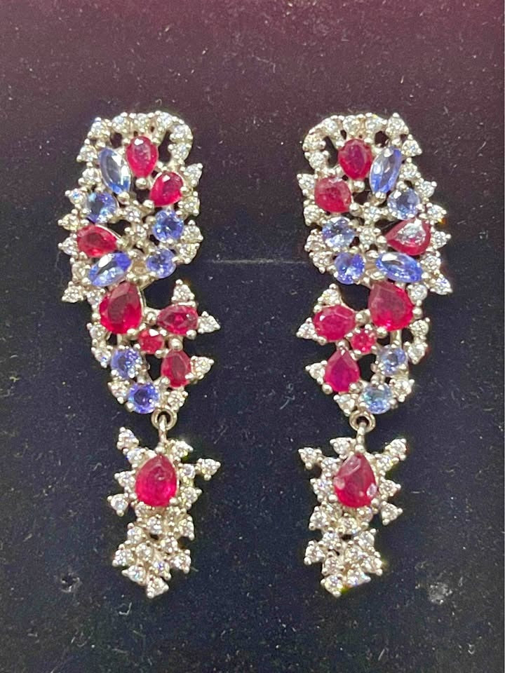 Colorful gemstone dangle earrings. The ornate design features vibrant red ruby and blue tanzanite stones in a cluster setting.