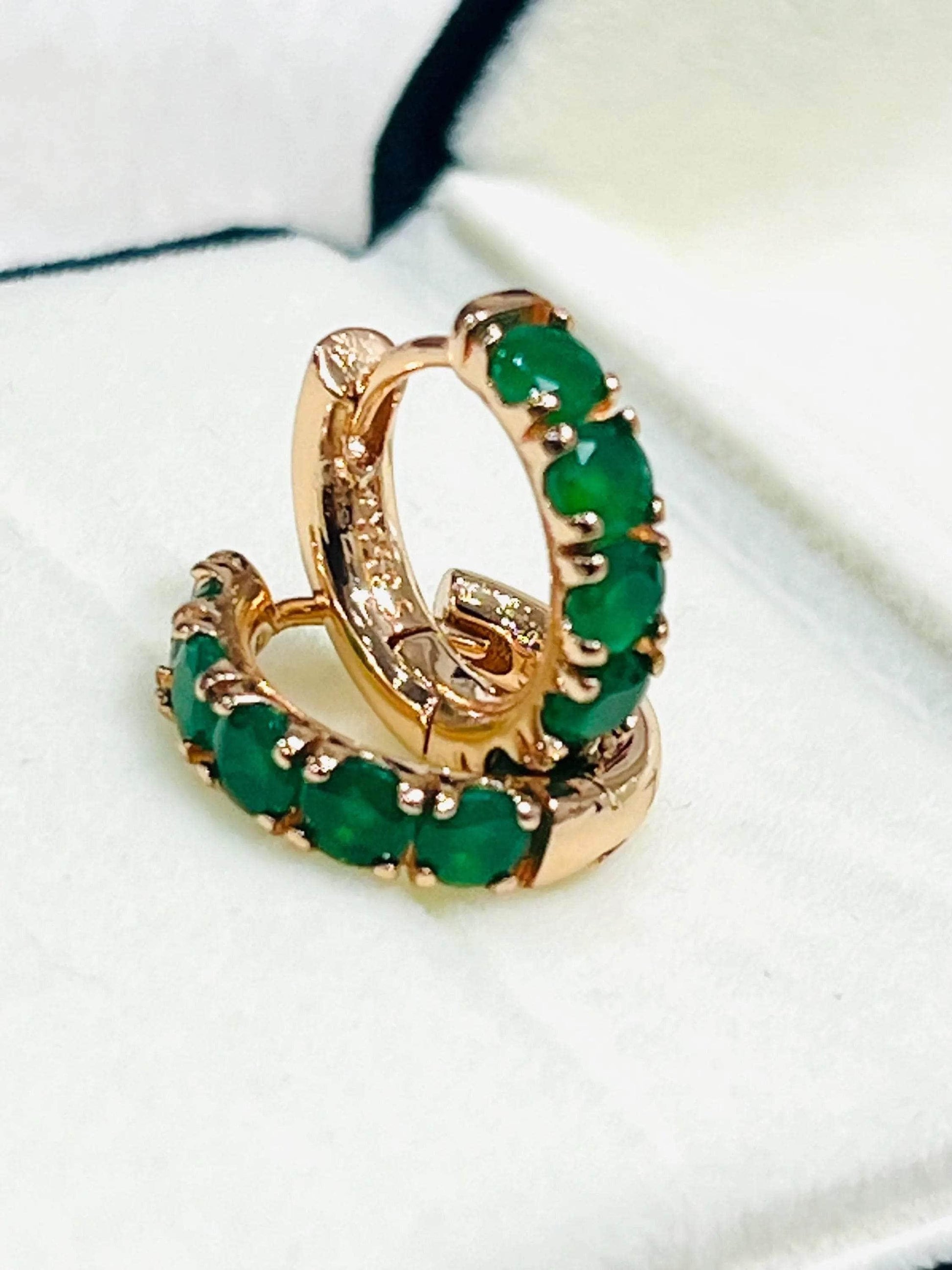 Pair of dainty round-cut emerald hoop earrings in lustrous rose gold, presented in a jewelry box.