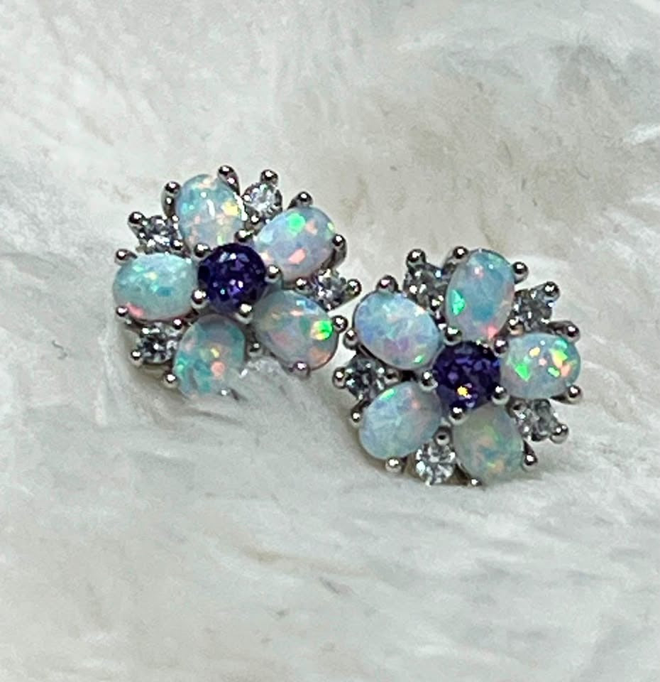 Pair of dainty fire opal and amethyst flower stud earrings with a vibrant play of color, on a soft white background.
