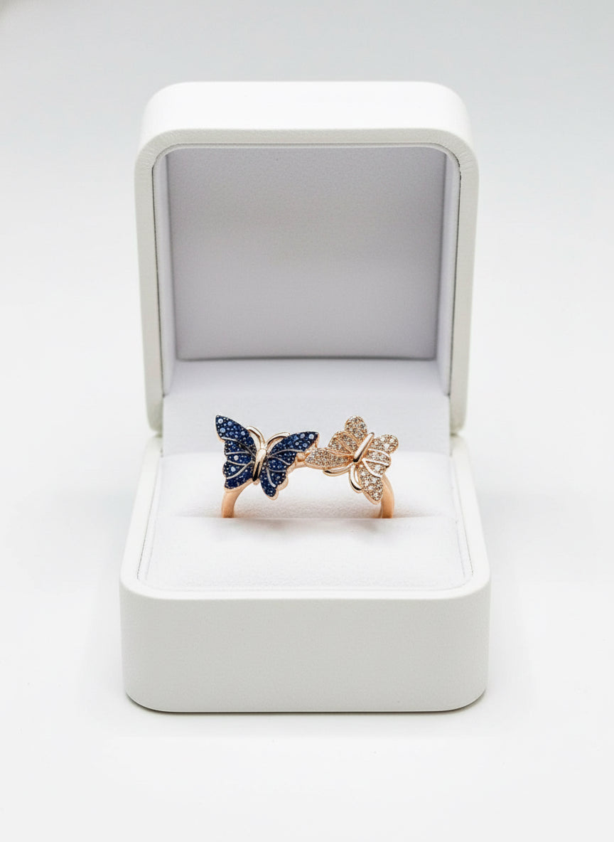 Elegant rose gold ring featuring intertwining blue and clear pave butterfly designs, in a wooden box.