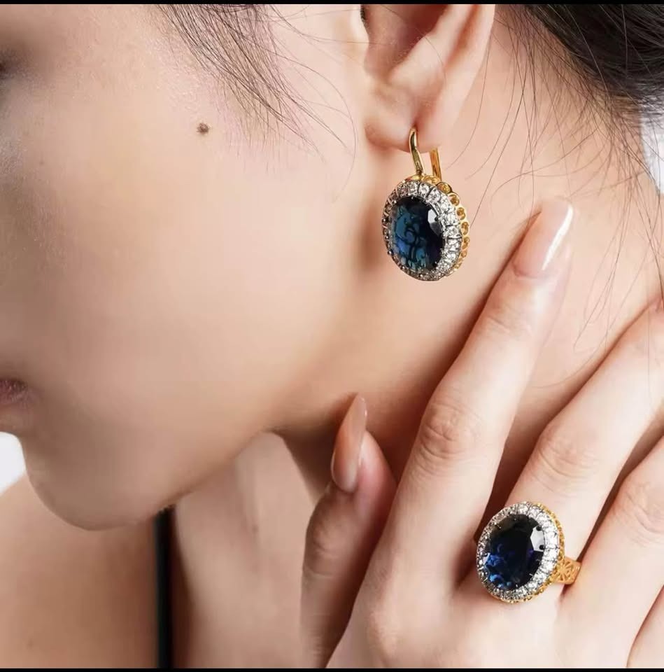 Model wearing elegant blue sapphire earrings and matching ring with diamond halo in gold setting.