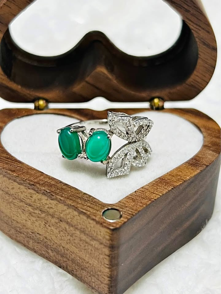  Exquisite sterling silver ring with natural emeralds and a sparkling butterfly design, displayed in a wooden heart box.