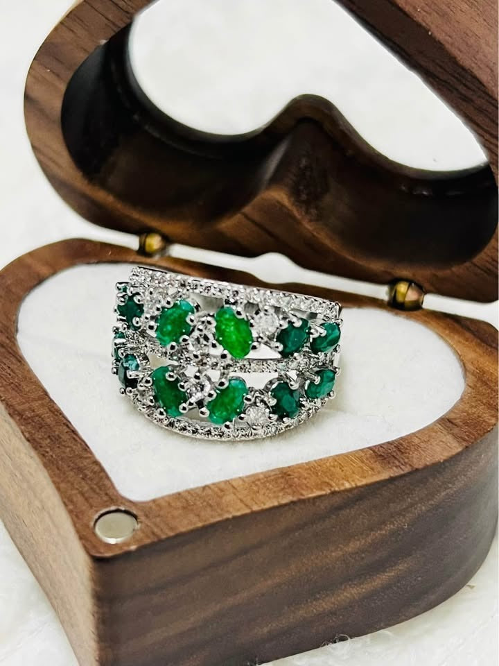 Elegant sterling silver ring with natural emeralds and delicate diamond accents, showcased in a wooden jewelry box.