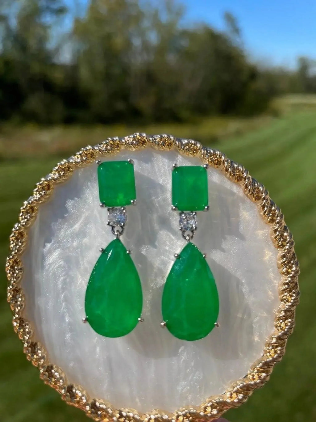 Pear-shaped emerald doublet earrings with rectangular tops, showcased in a natural outdoor setting.