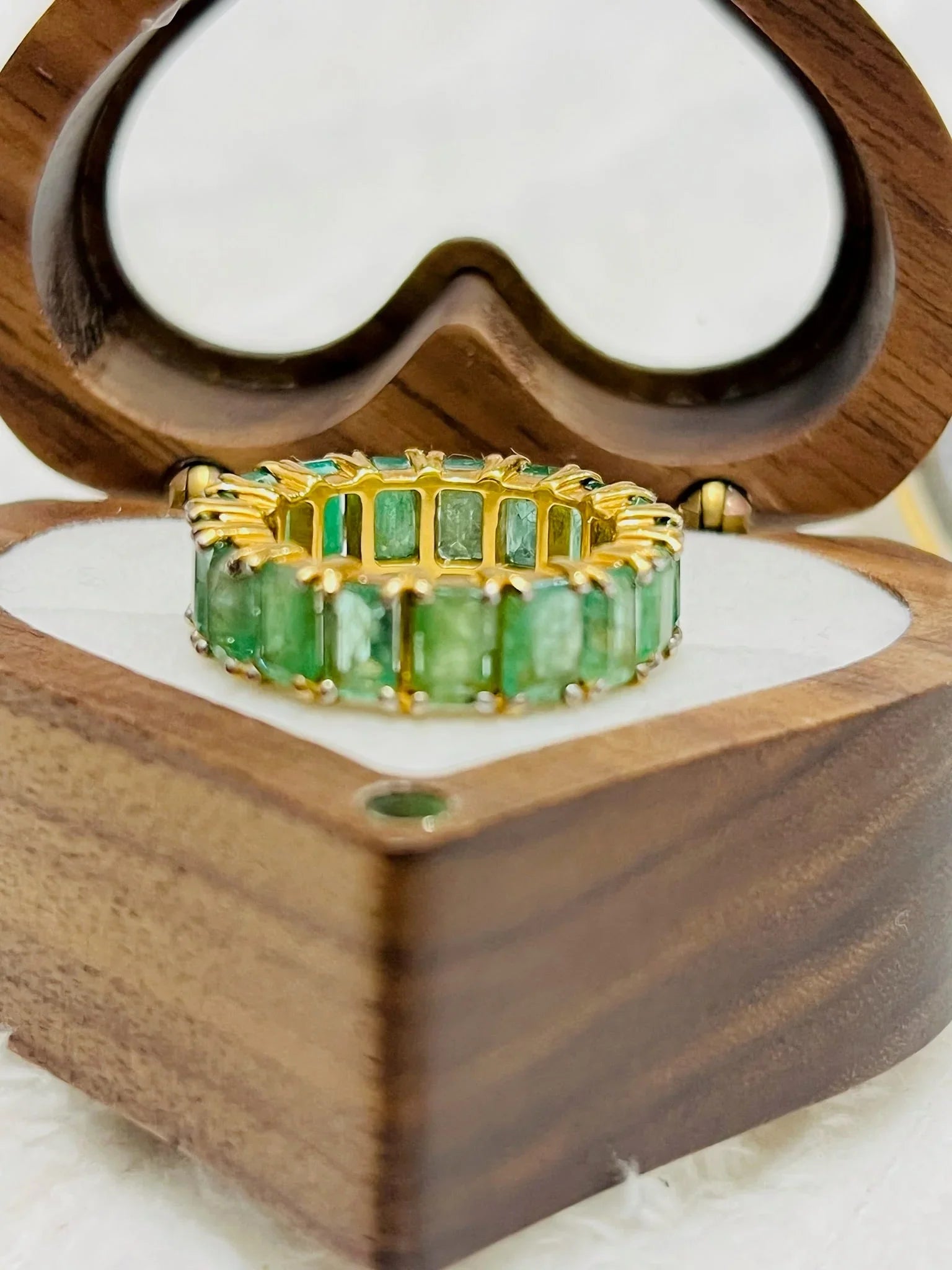 Close-up of an emerald eternity band in gold vermeil, nestled in a charming heart-shaped wooden box.