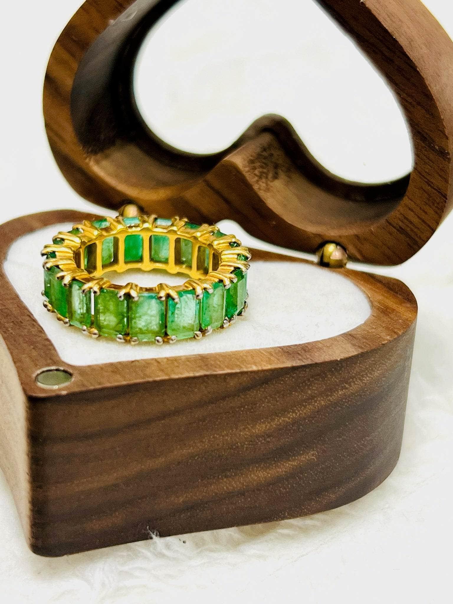 Gold vermeil emerald eternity band gleaming inside an open heart-shaped wooden jewelry box.