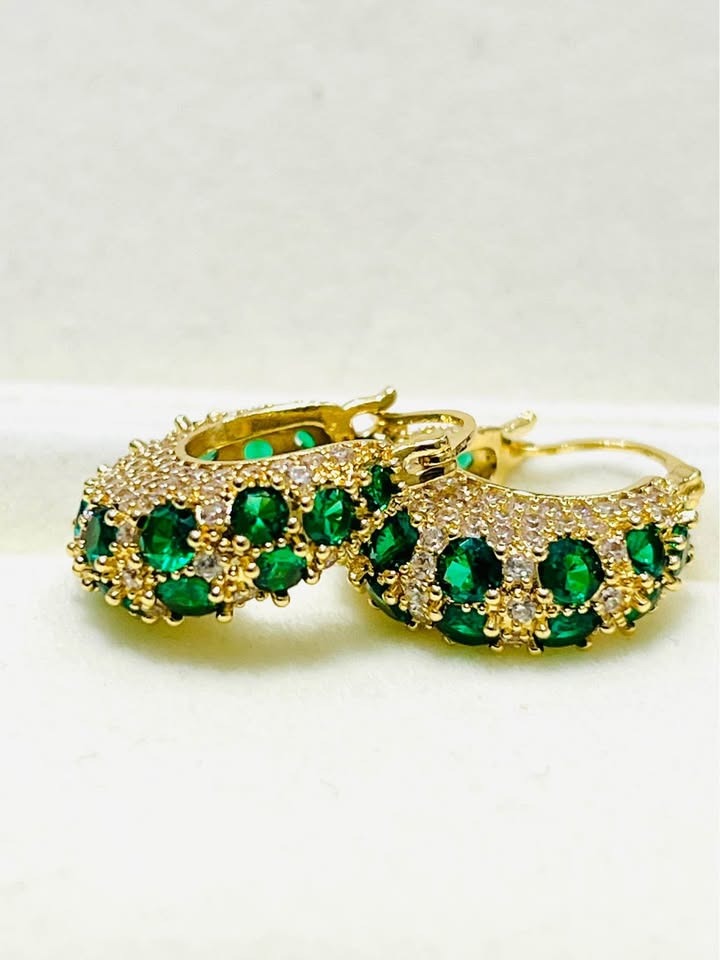 Close-up of gold filled hoop earrings set with vibrant emerald green zircons and clear stones.