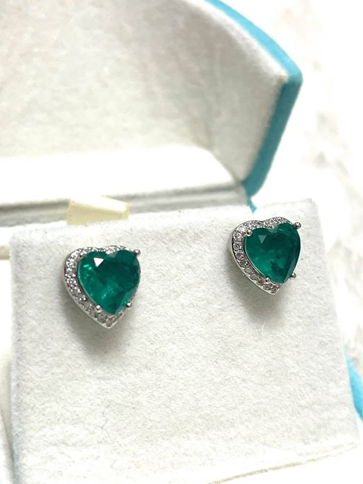  Heart-shaped Zambian emerald doublet earrings with diamond halos on a white display stand.