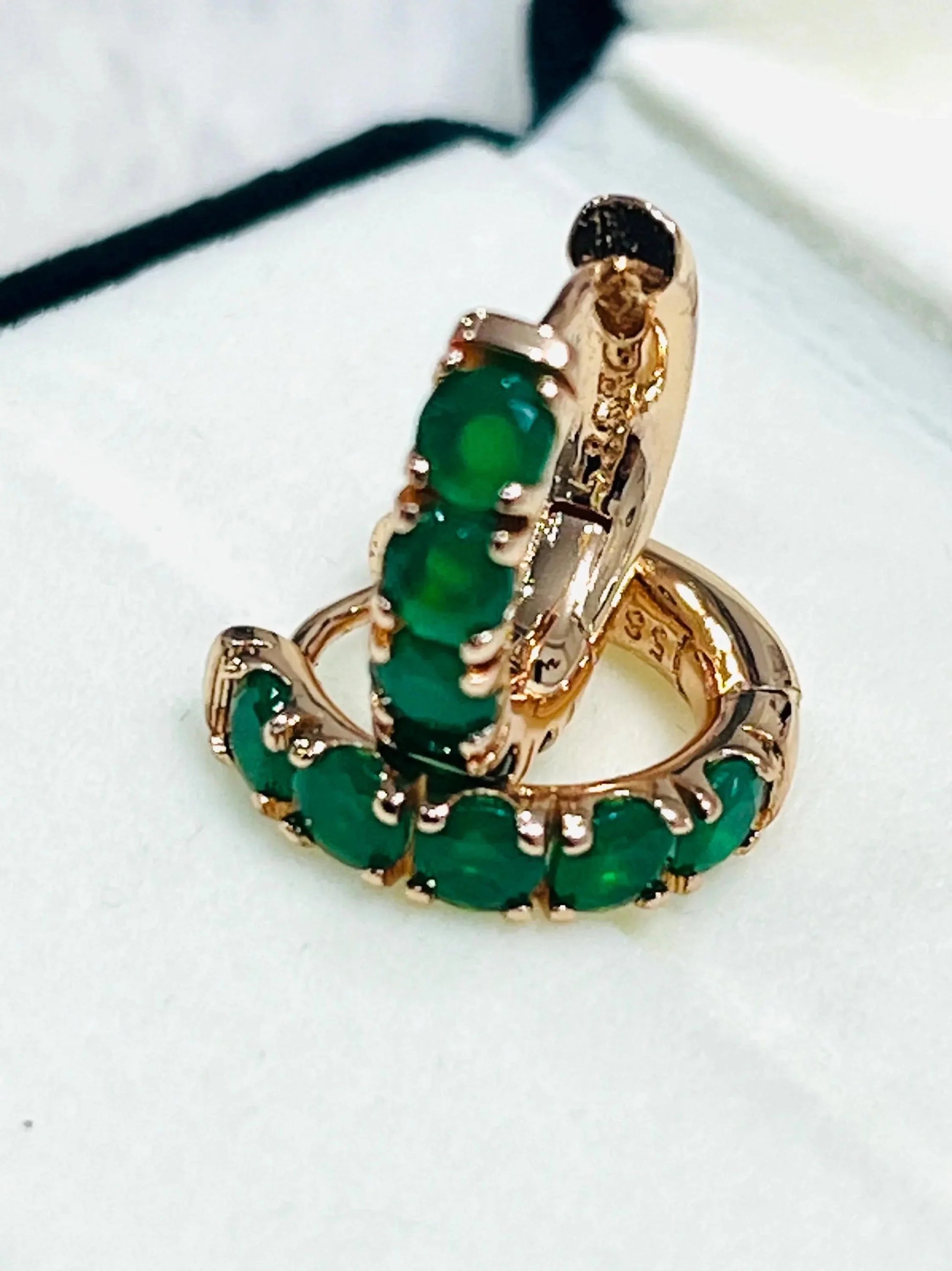 Stacked view of dainty round-cut emerald hoop earrings in rose gold, emphasizing their delicate design.