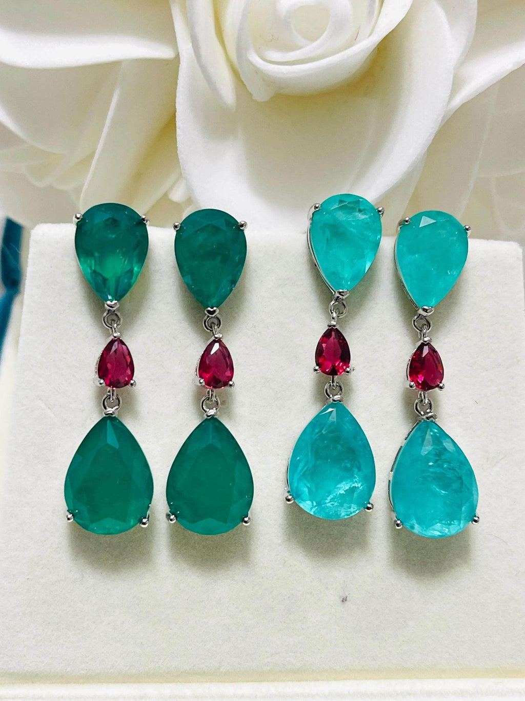 Two pairs of elegant emerald and Paraiba doublet drop earrings with ruby accents, displayed beautifully.