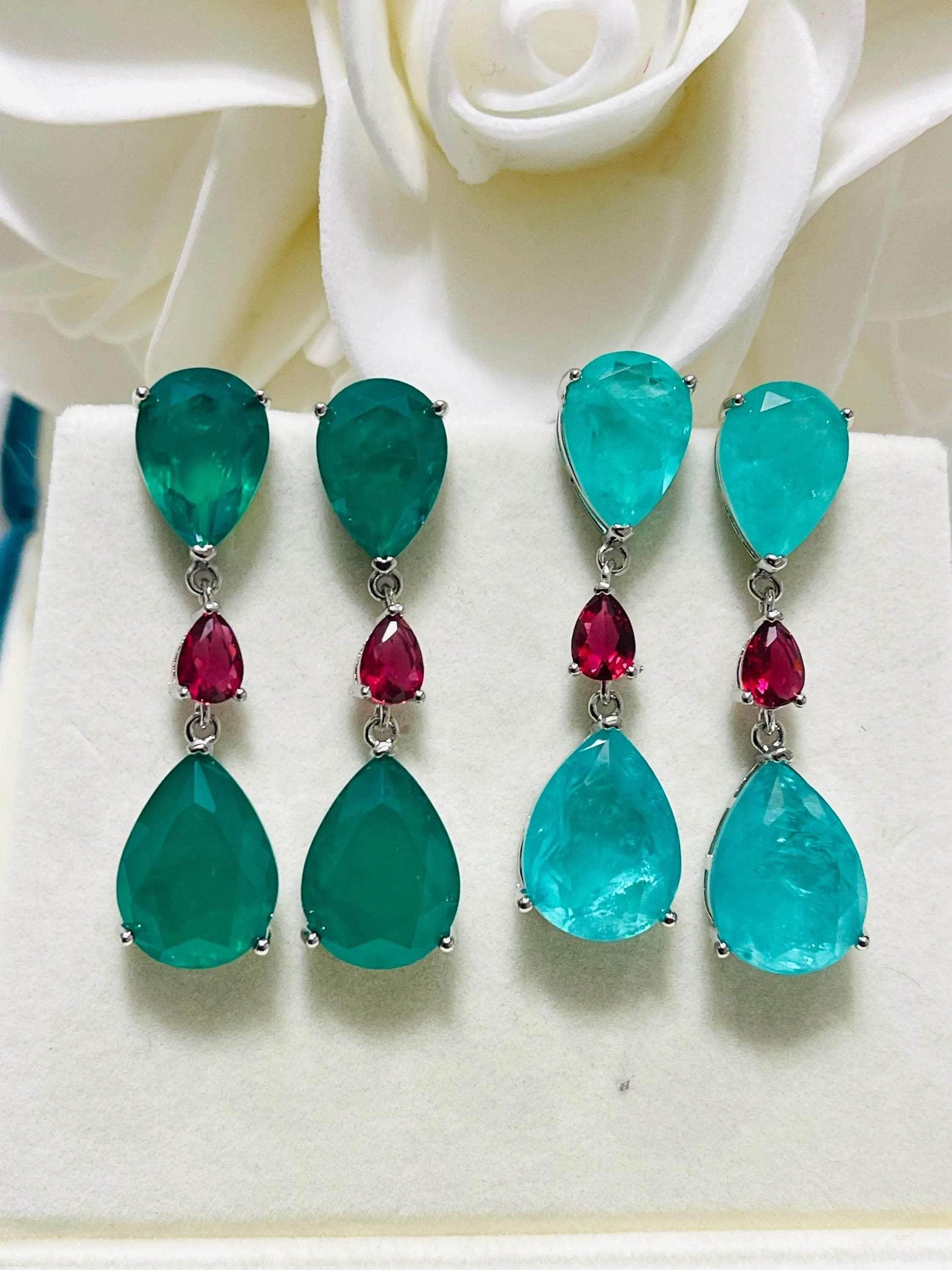 Two pairs of elegant emerald and Paraiba doublet drop earrings with ruby accents, displayed beautifully.