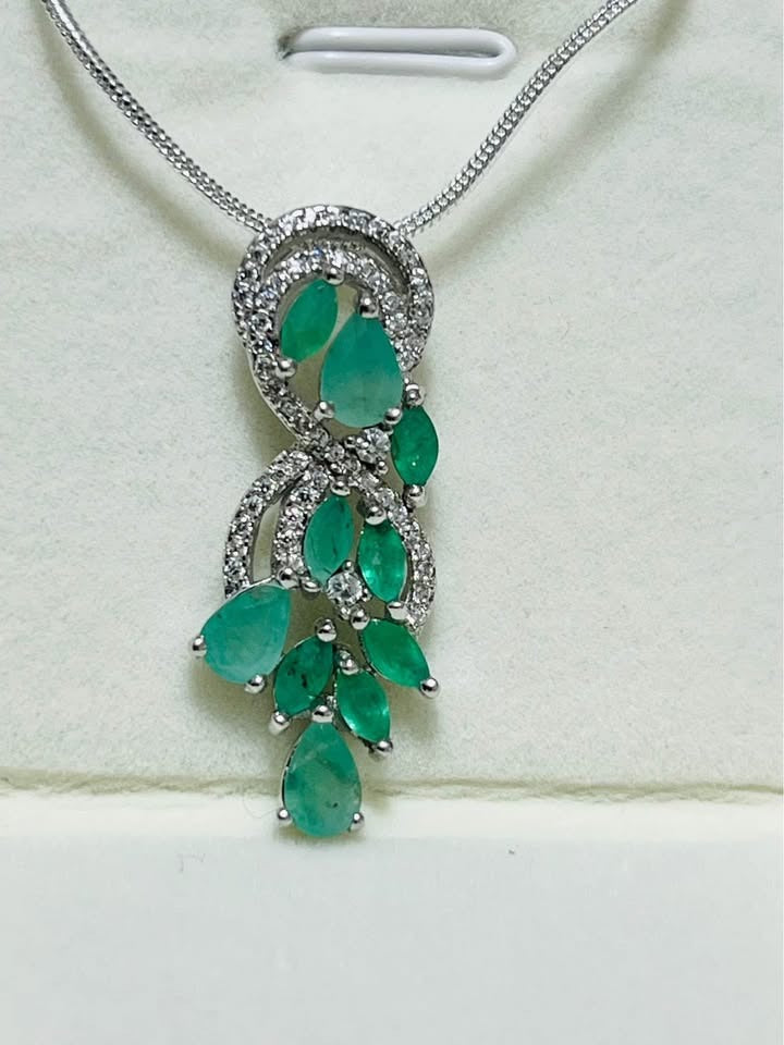 Detailed close-up of a natural Colombian emerald and diamond pendant necklace, highlighting the vibrant green emeralds.