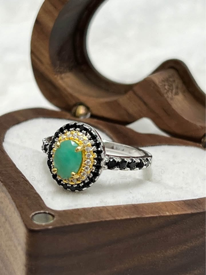 Side view of sterling silver emerald ring with black spinel and two-toned gold accents.
