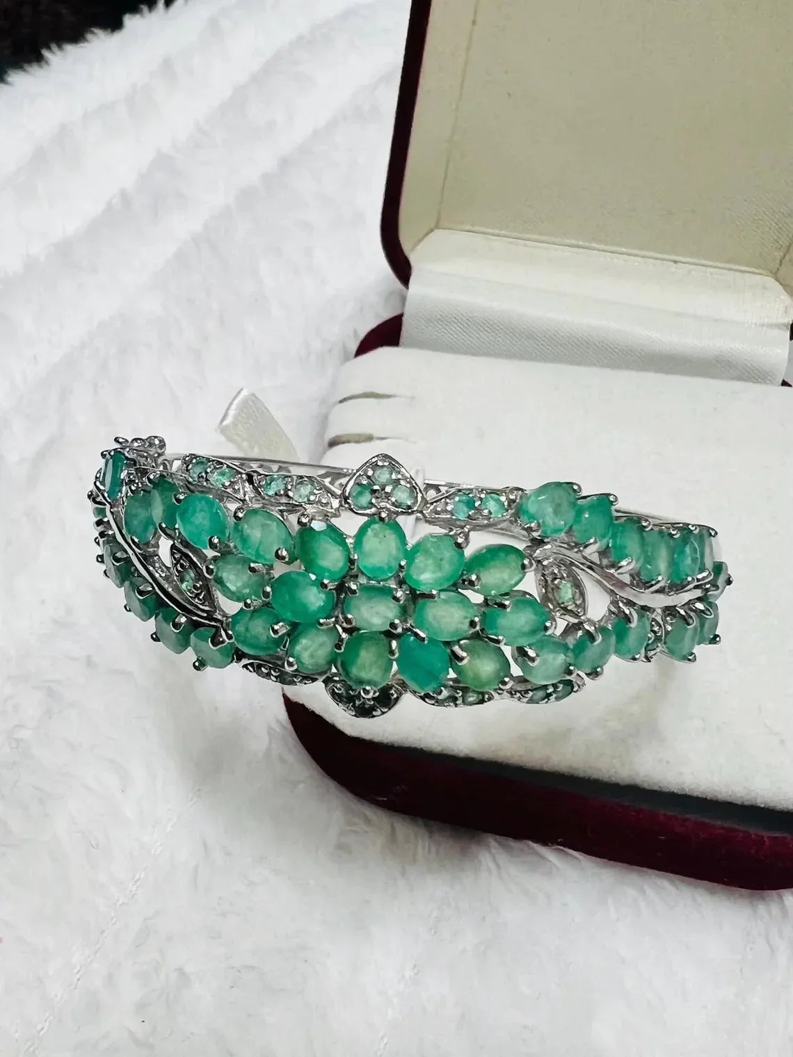 Close-up of an Emerald and Tanzanite floral bangle, emphasizing the lush green stones and silver setting.