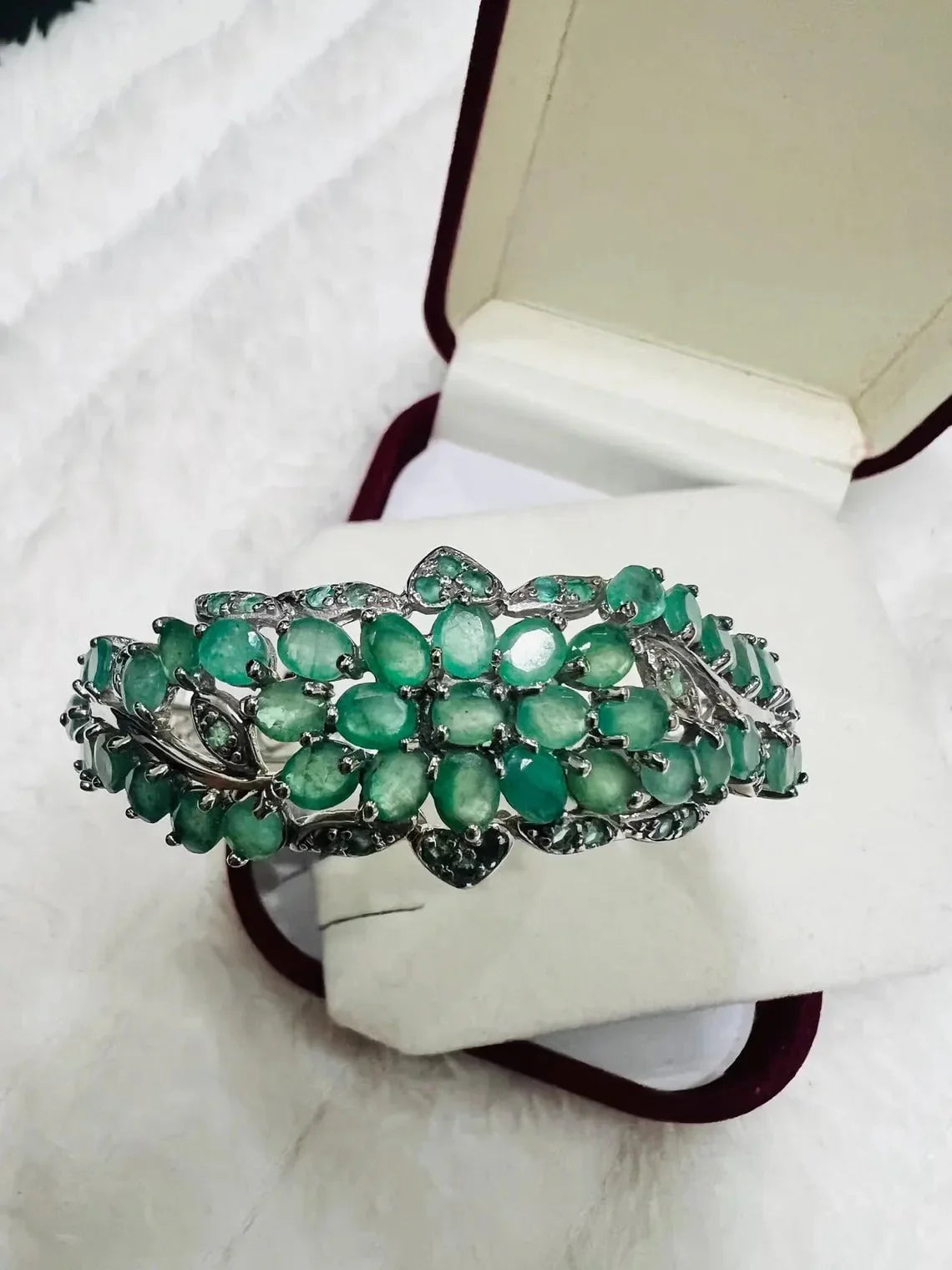 Exquisite sterling silver floral bangle with natural emeralds and tanzanites, displayed in a jewelry box.