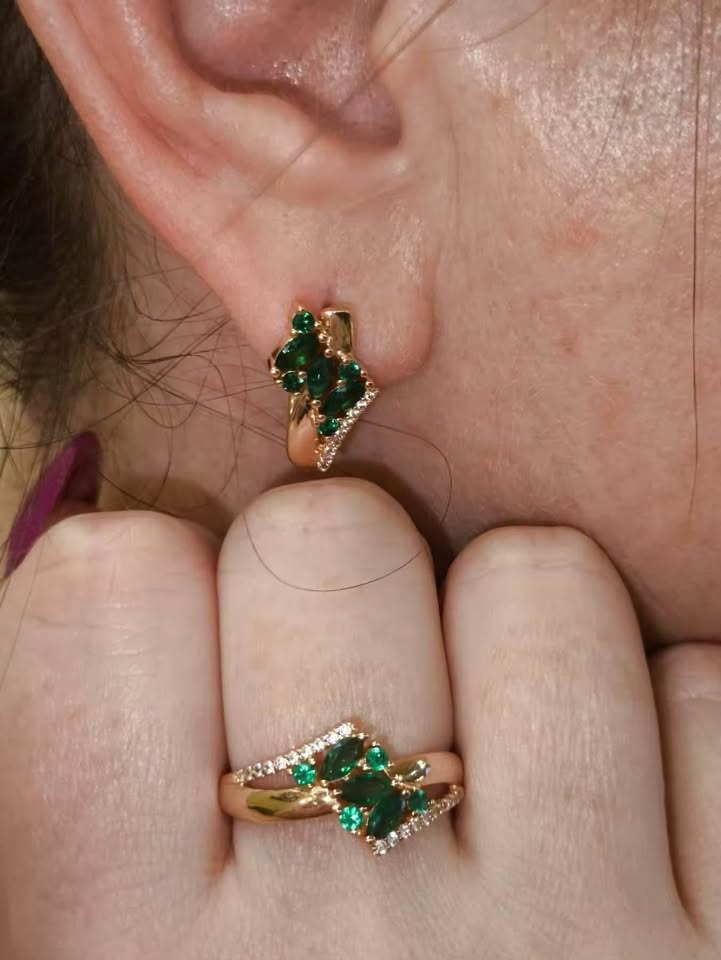 A model wearing a 14k rolled gold ring and earrings set, featuring vibrant emerald green stones.