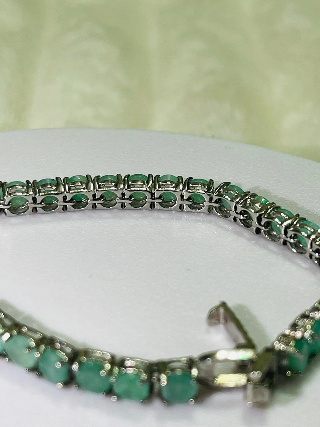  Close-up detail of a silver emerald tennis bracelet, focusing on the individual gemstone settings and the secure box clasp.