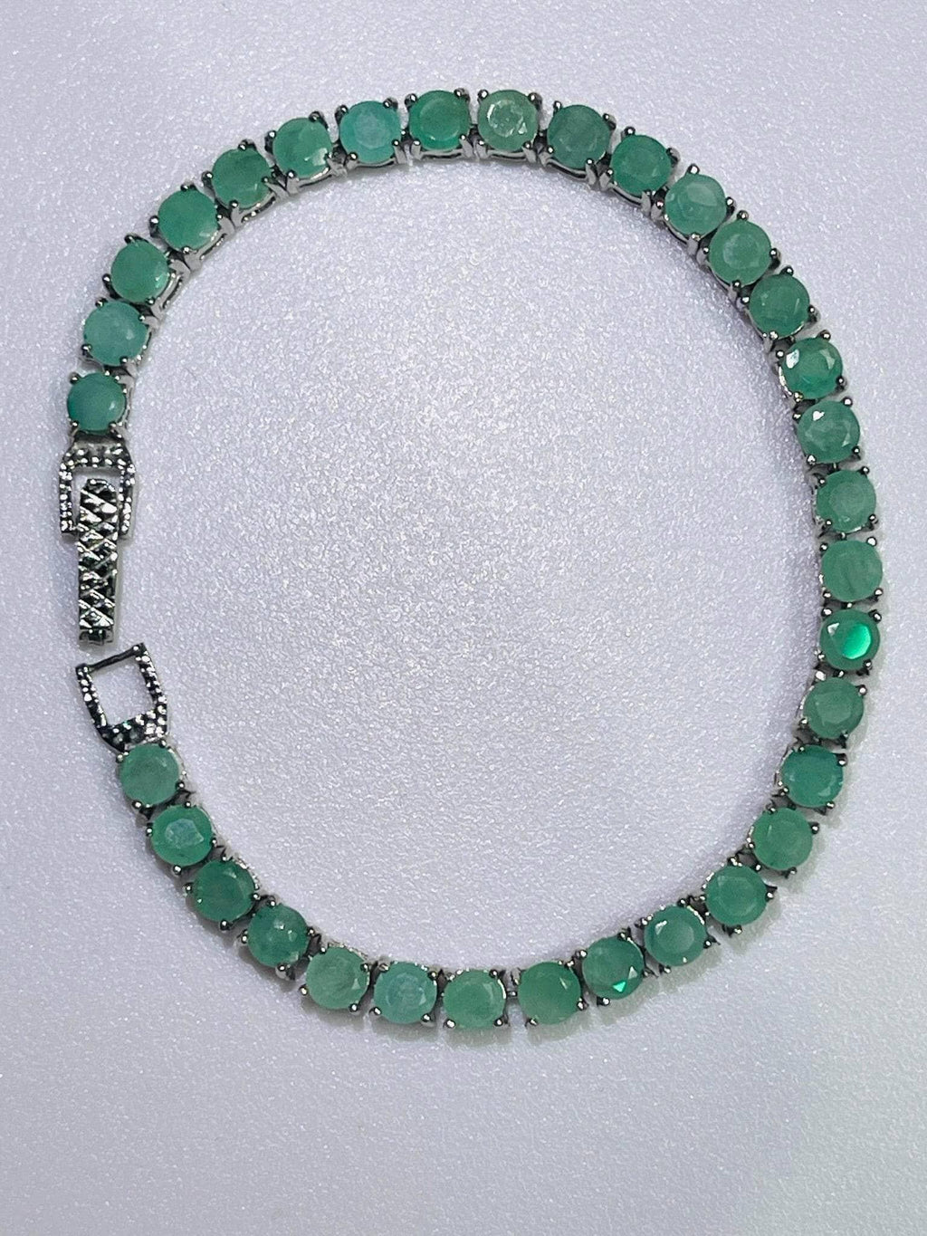 Full overhead view of a sparkling silver tennis bracelet forming a circle, set with continuous round-cut emerald gemstones.