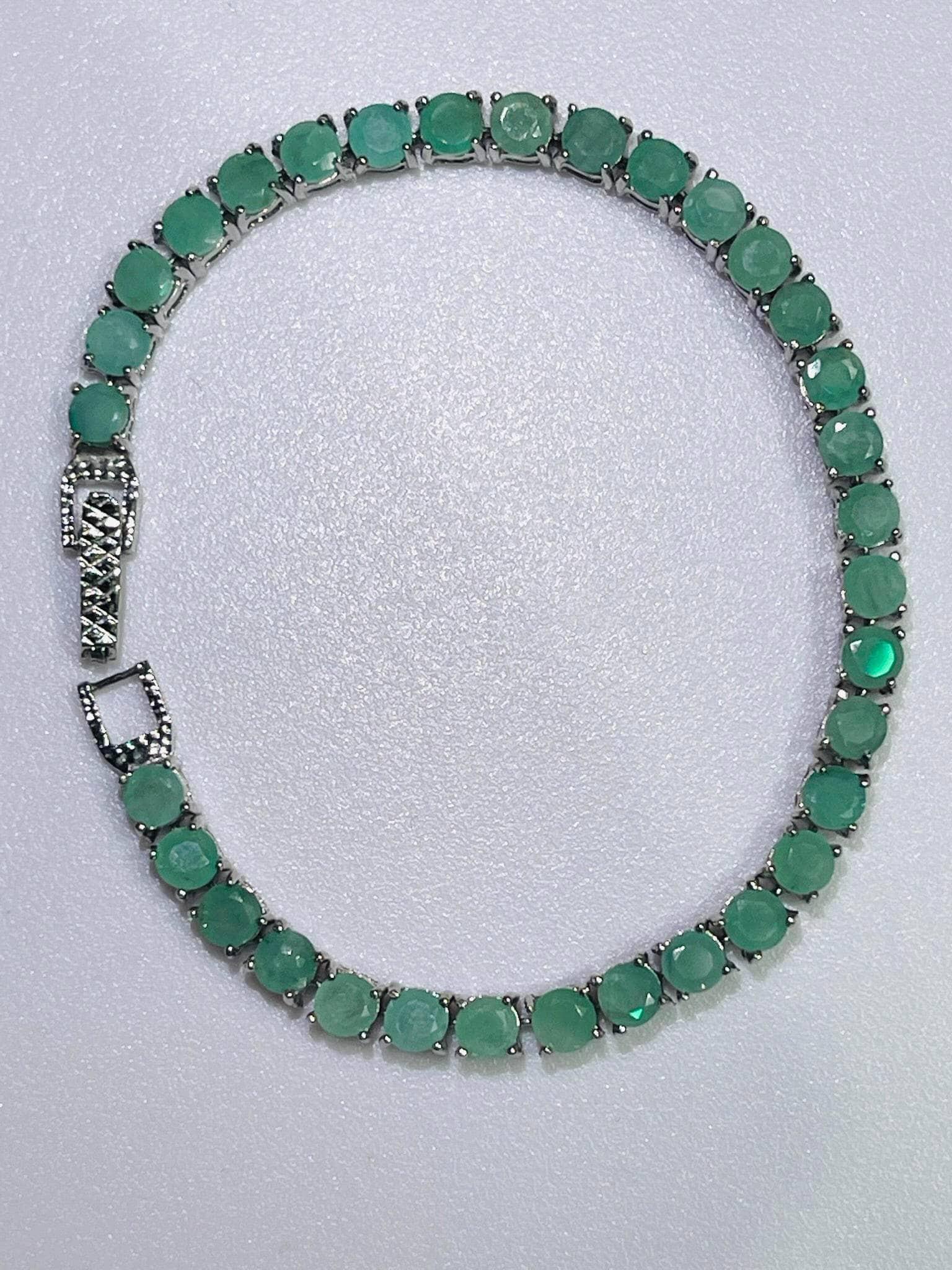Full overhead view of a sparkling silver tennis bracelet forming a circle, set with continuous round-cut emerald gemstones.