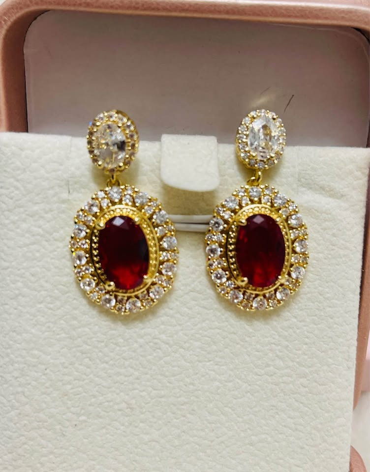 Close-up of fancy gold-plated earrings, highlighting the detailed leaf and branch motif on a simple white background.