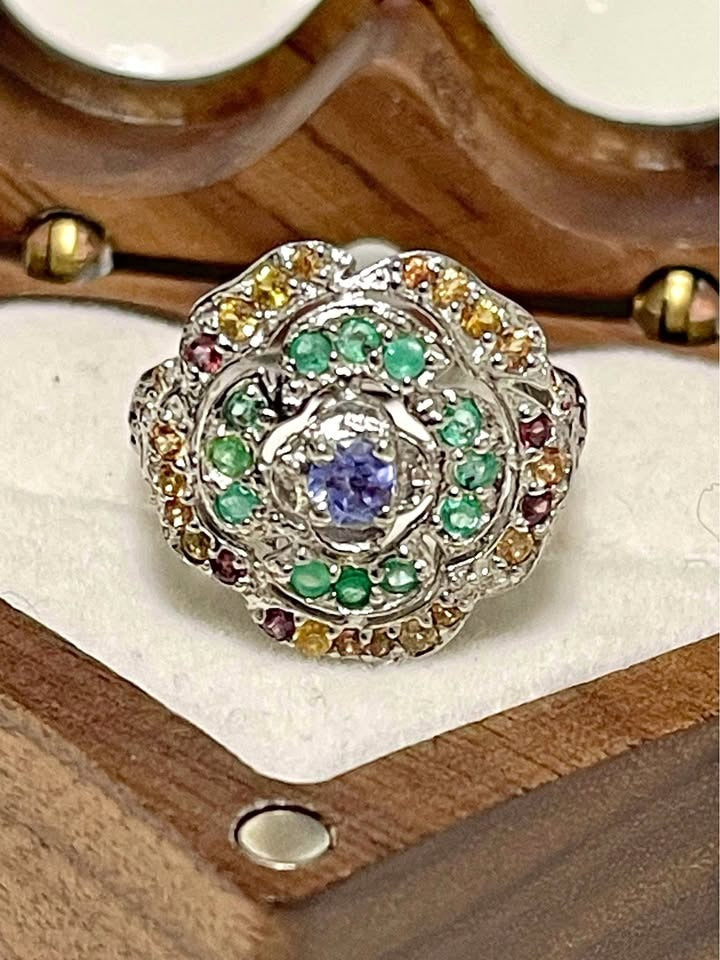 A vibrant floral cluster ring. The design highlights a central tanzanite surrounded by emerald and peridot gemstones.