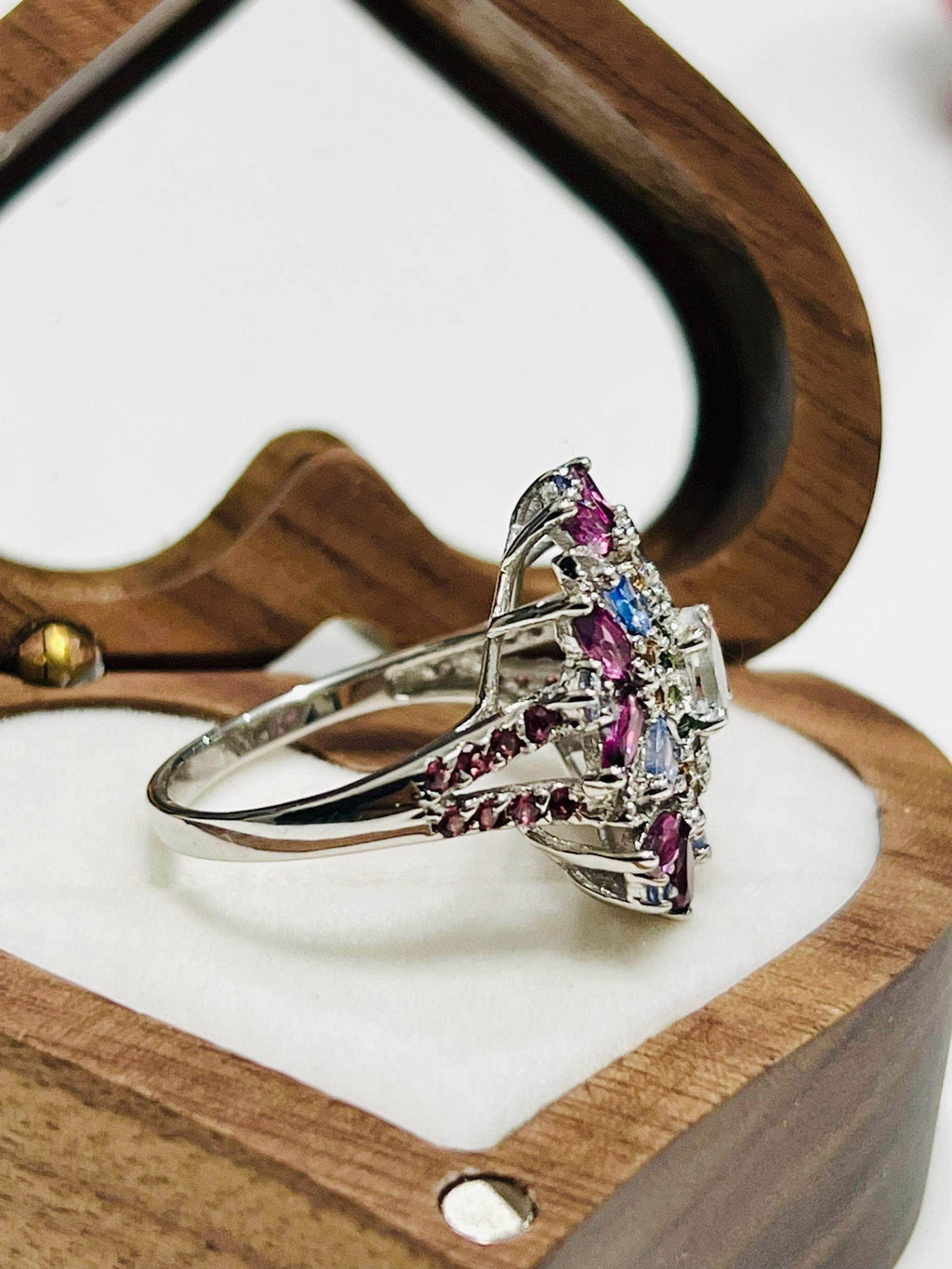 Side view of a unique floral ring featuring aquamarine, garnet, and tanzanite in a decorative setting.
