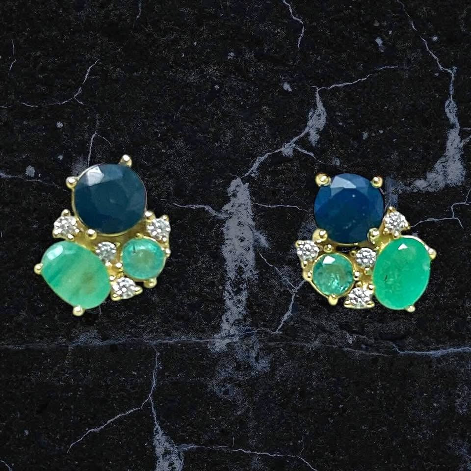 Natural Colombian emerald and blue sapphire cluster earrings on a dark marble background.