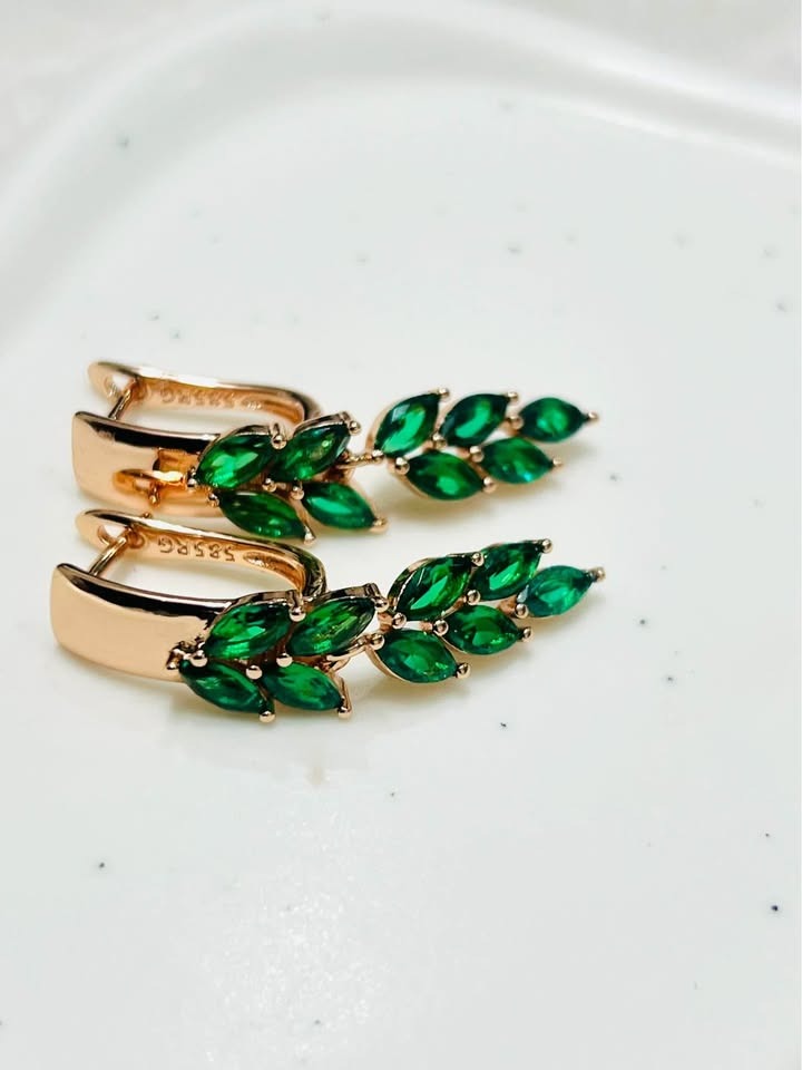 Close-up of 14k gold-filled earrings with brilliant green topaz stones set in a stunning leaf motif, modern jewelry.