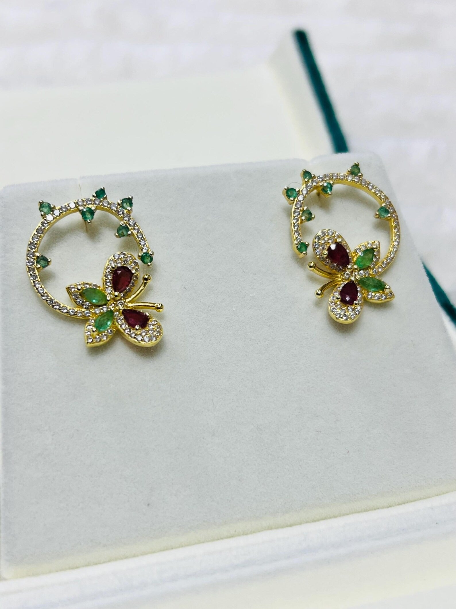 Gold-plated butterfly and flower earrings featuring vibrant ruby and emerald gemstones, presented beautifully.