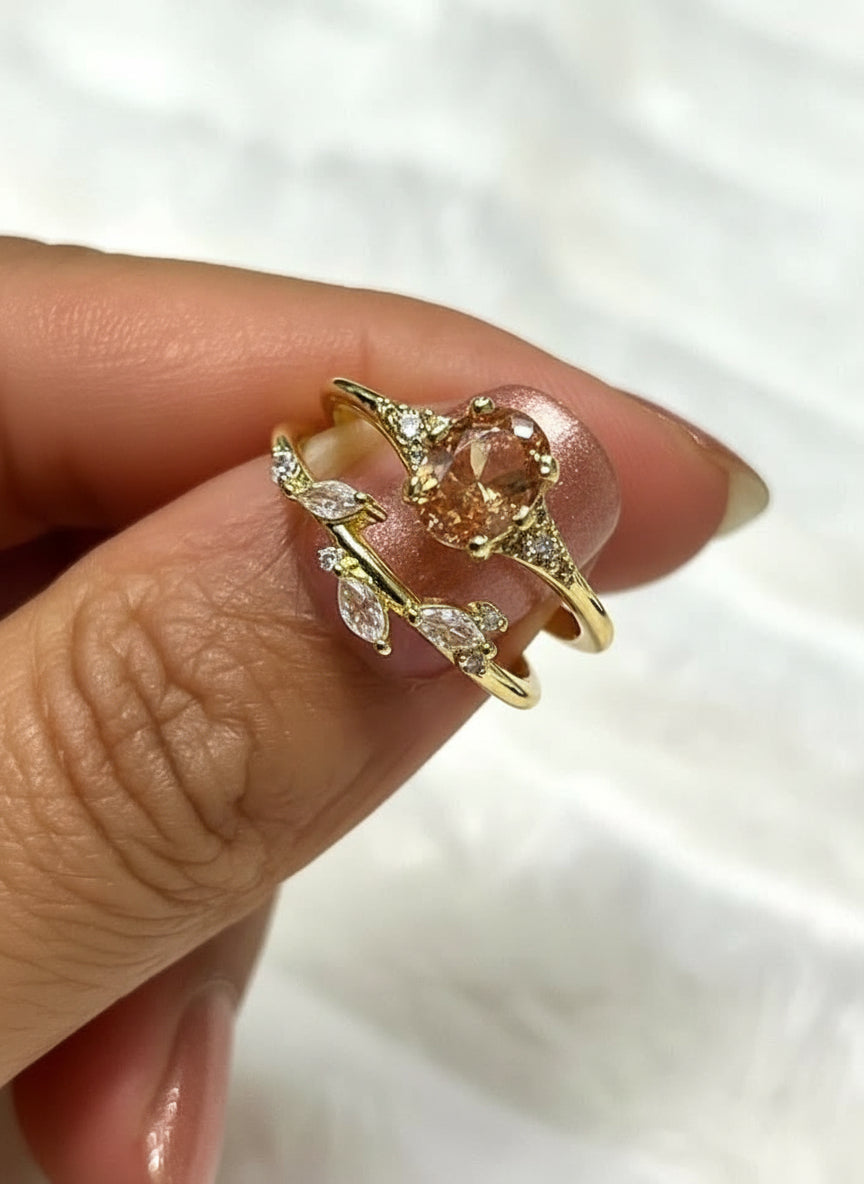 Duo ring set in gold tone with an oval orange gem and sparkling leaf accents, held gently.