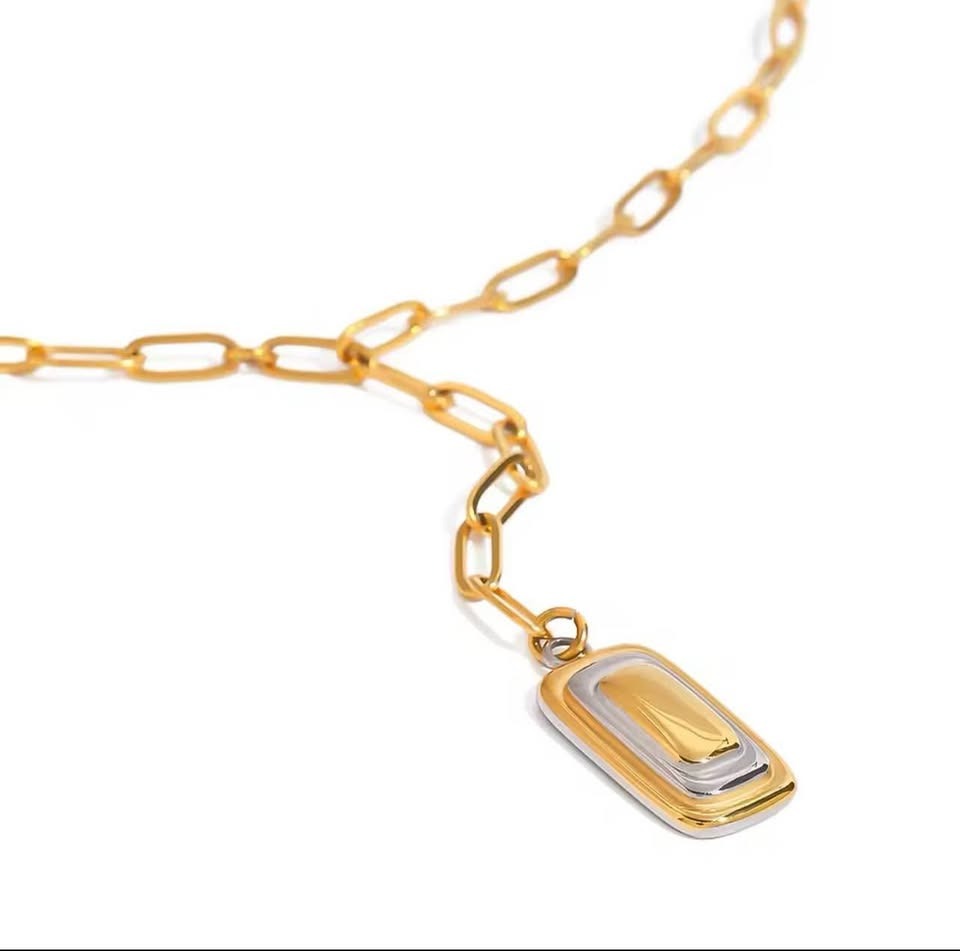 Close-up of 18K gold filled paperclip lariat chain with a two-tone rectangular pendant on white.