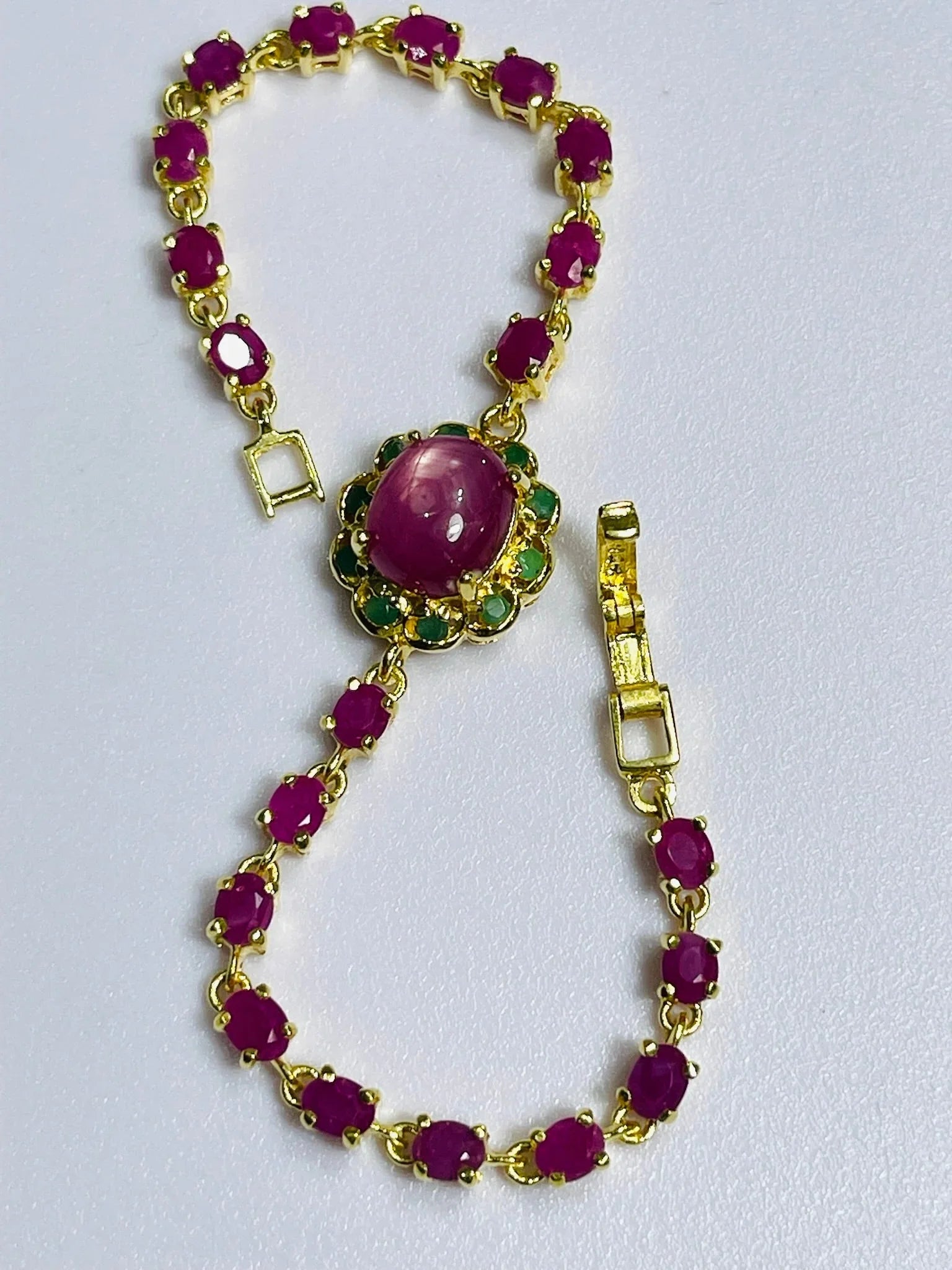 Exquisite gold bracelet with oval ruby gemstones and a central large ruby cabochon with emerald accents, unclasped for detail