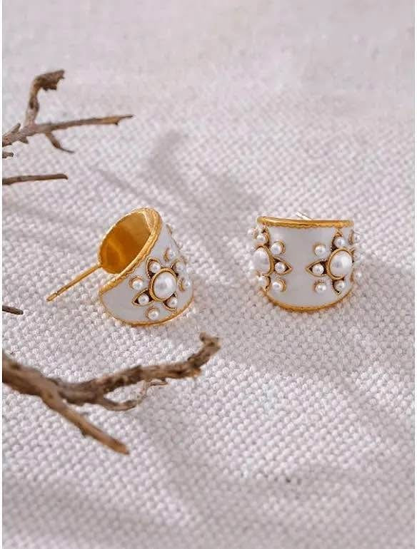 Two vintage gold vermeil hoop earrings with white enamel and pearl details, with a branch nearby.