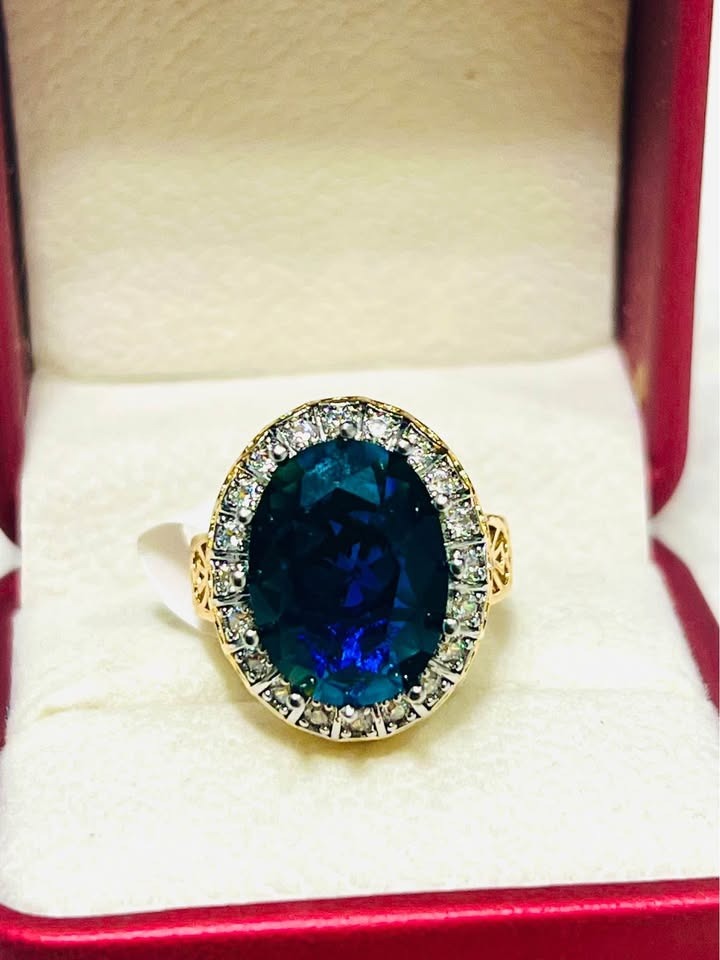 Grand oval blue sapphire and diamond halo ring, set in gold, presented in an open red jewelry box.