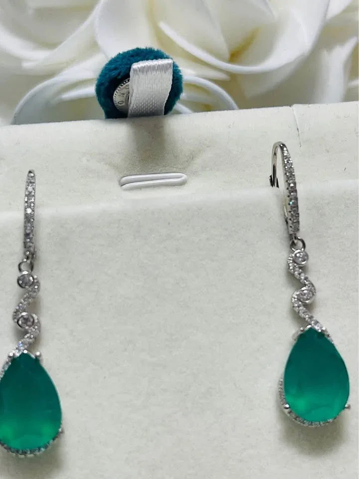A close-up of sterling silver earrings with green agate gems, resembling emeralds, against a white background.