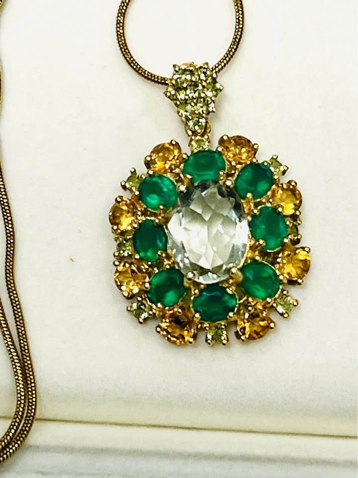  Close-up of a luxurious pendant necklace featuring a central green amethyst surrounded by colorful agate and sapphire.