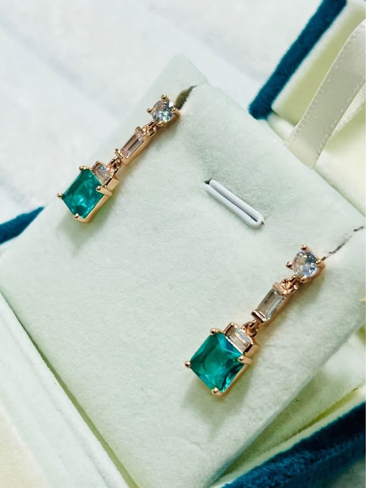 Angled view of striking sterling silver, rose gold-filled green topaz earrings with baguette and round stones.