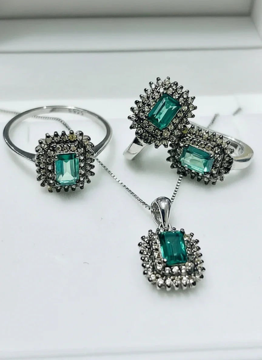 A collection of green tourmaline and diamond jewelry pieces, including rings and a pendant on a white surface.
