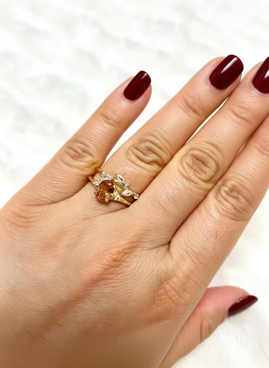 Hand wearing a gold-tone duo ring set featuring an oval orange gem and a delicate leaf design.