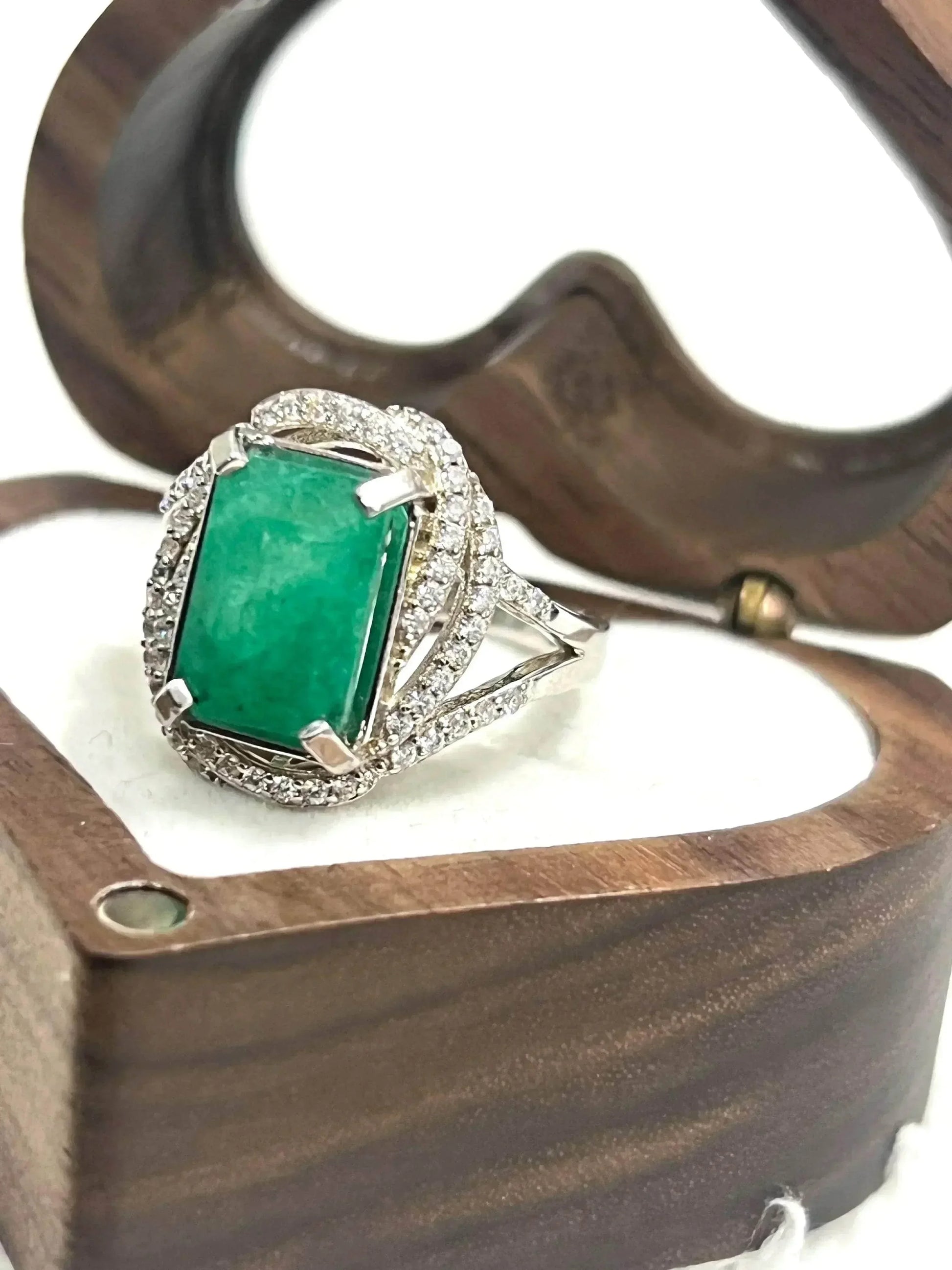 Side view of a dazzling handcrafted emerald ring with CZ accents, presented in a unique wooden heart box.