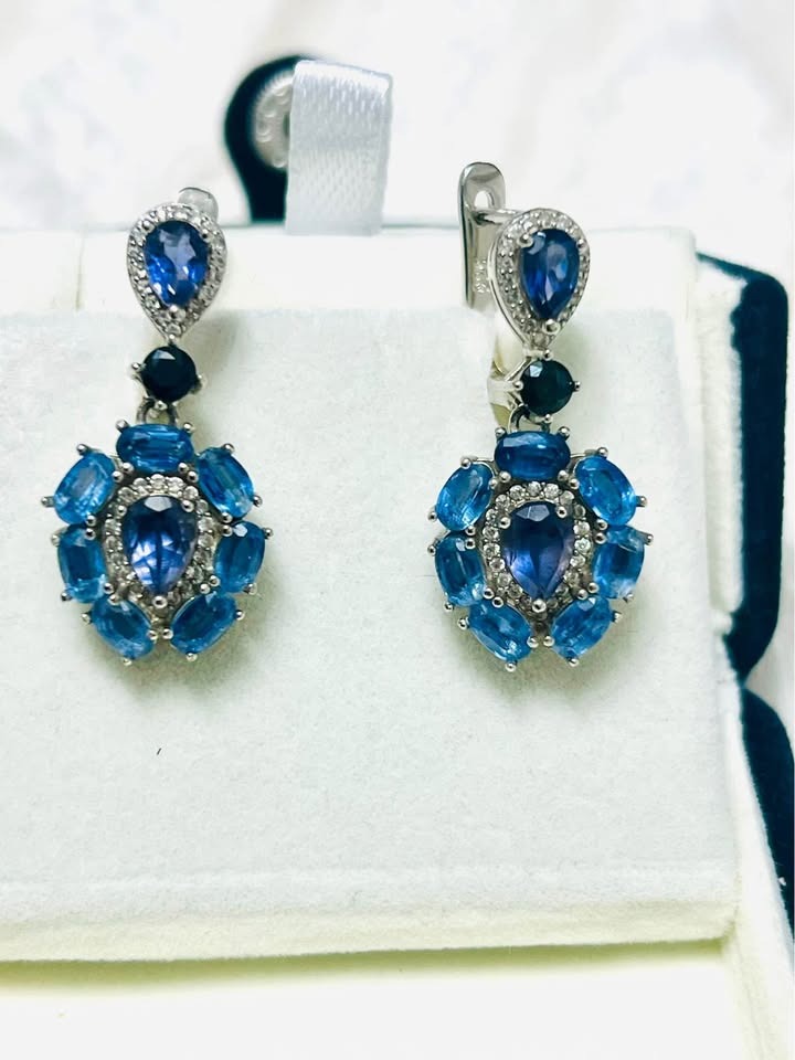 A pair of handmade blue gemstone dangle earrings, featuring sapphires and iolites, presented in a white jewelry box.