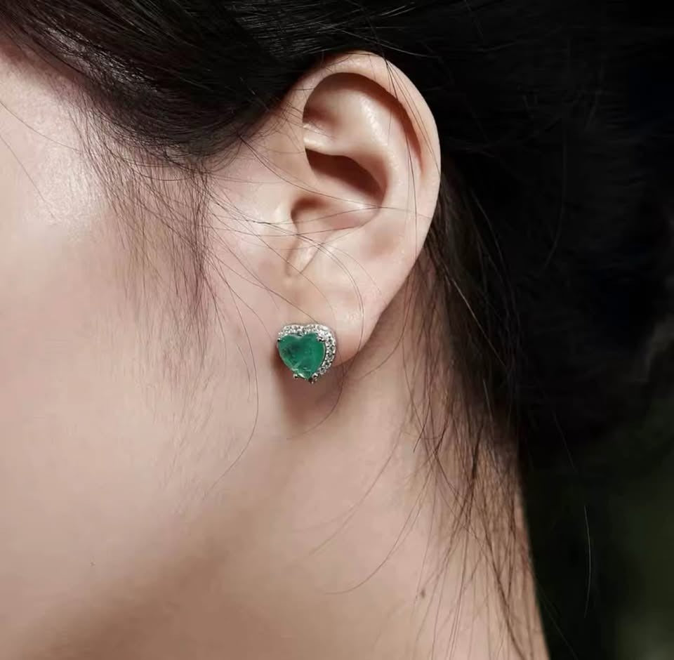  Close-up of a heart-shaped Zambian emerald doublet earring with sparkling halo, worn on an ear.