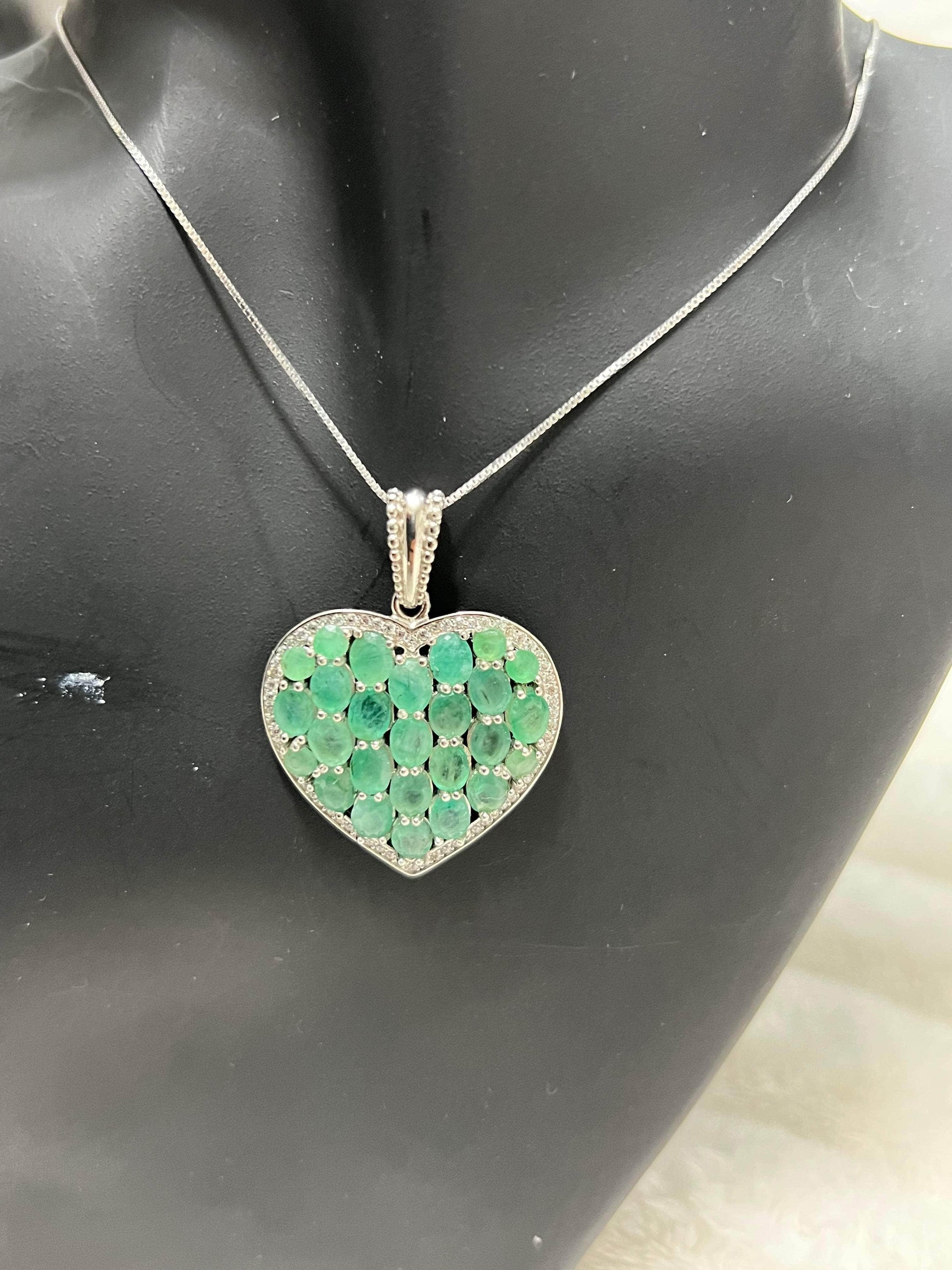 Heart-shaped 925 sterling silver pendant adorned with natural Colombian emeralds and diamonds, presented on a dark display.