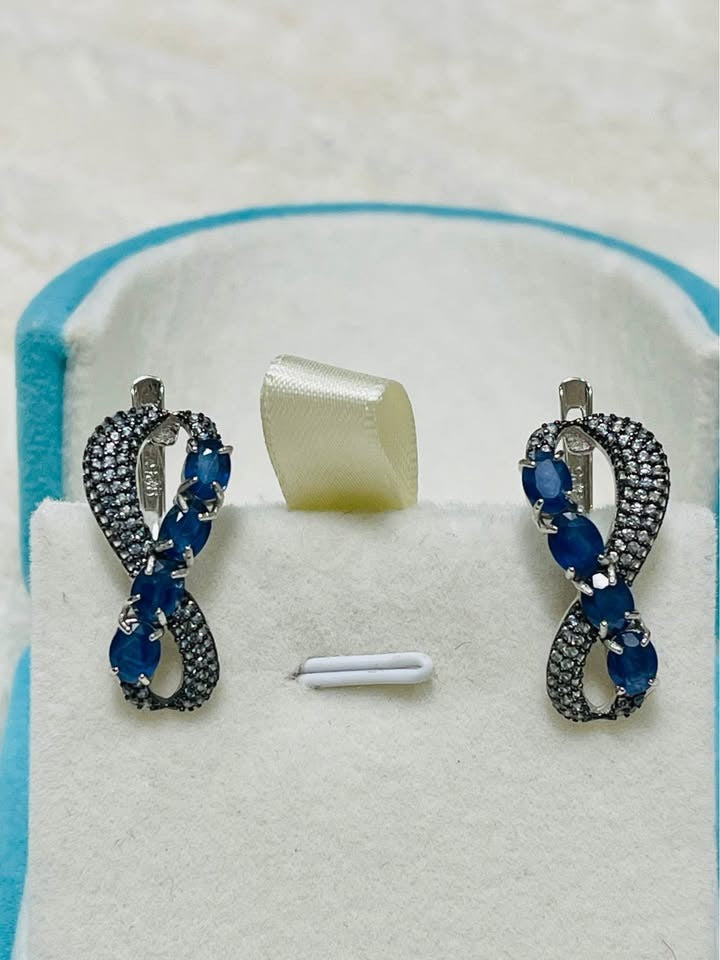 Pair of exquisite infinity design stud earrings featuring vibrant blue sapphires.