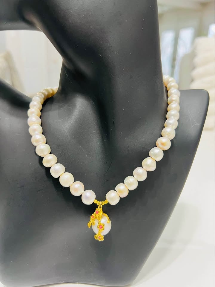 A natural large pearl necklace with a pink ruby and gold-plated pendant, displayed on a mannequin.