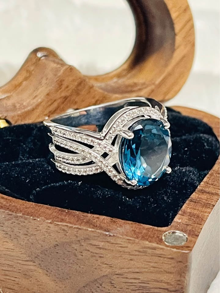 Angled view of an oval London Blue Topaz ring with diamond detailing, presented in a decorative box.