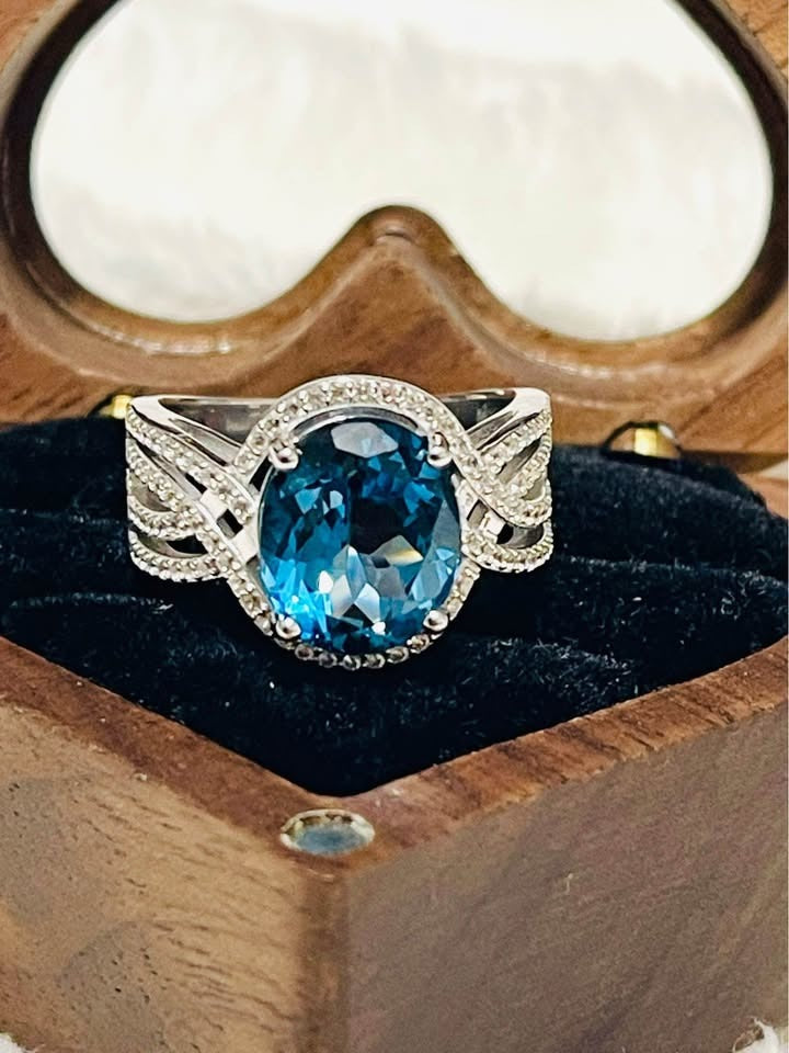  Close-up of an exquisite London Blue Topaz and diamond ring, shimmering within a heart-shaped box.